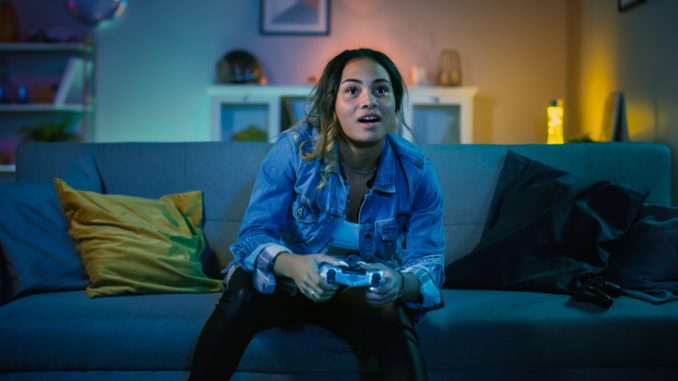 Beautiful Excited Young Black Gamer Girl Sitting on a Couch and Playing Video Games on a Console. She Plays with a Wireless Controller. Cozy Room is Lit with Warm and Neon Light. Twitter, le reseau social annonce les pays qui parlent le plus de jeux video
