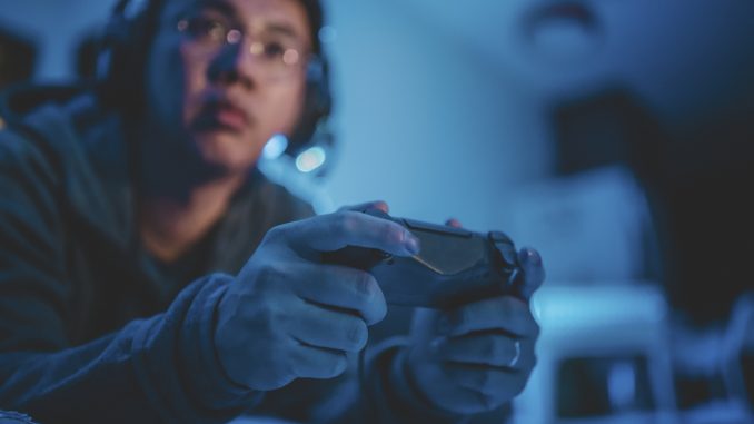 an asian chinese mid adult playing video games at home alone at night in darkness with headset and game controller sitting on sofa lying down Valorant, le jeu video multijoueur est l un des jeux les plus tendance