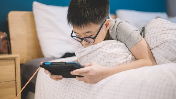 an asian chinese boy playing on his digital tablet on bed during weekend Jeux video et addiction des mineurs, la Chine impose une reglementation