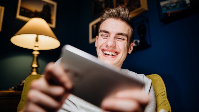 jeux-video-gamer Un jeune homme qui sourit en jouant sur son smartphone