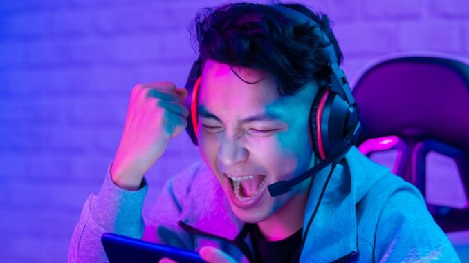 Twitch-fonctionnalite-recolte-don Jeune homme enthousiaste avec son smartphone et son casque