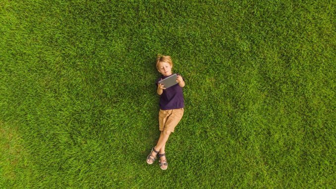 enfant-jeux-video Petit garçon allongé sur l’herbe et regardant une tablette