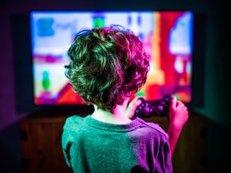 Un jeune garçon, manette à la main, jouant à un jeu vidéo ultracoloré sur un large moniteur TV.
