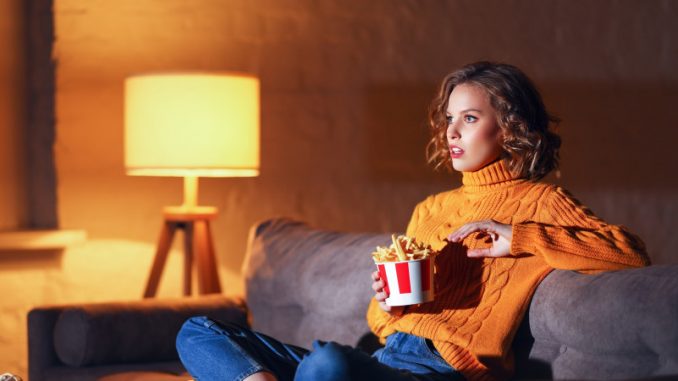 contenu-culturel-dematerialise-stremaing-illegal-abonnement payant Une jeune femme sur son sofa en train de visionner un contenu culturel dématérialisé de type vidéo.