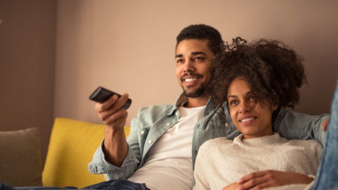 mesure-d-audience-mediametrie-plateformes-streaming Un couple installé dans un sofa visionnant un contenu vidéo, dont l’audience est ou sera mesurée par Médiamétrie.