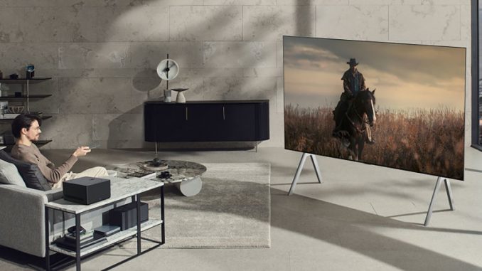 tv-sans-fil-m3-lg La TV sans fil LG installée dans un salon au style moderne avec un homme aux commandes.
