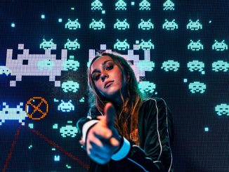 La DJ Mariana BO ayant travaillé avec le label Beat Drop postée devant l’écran d’une version du jeu Space invaders