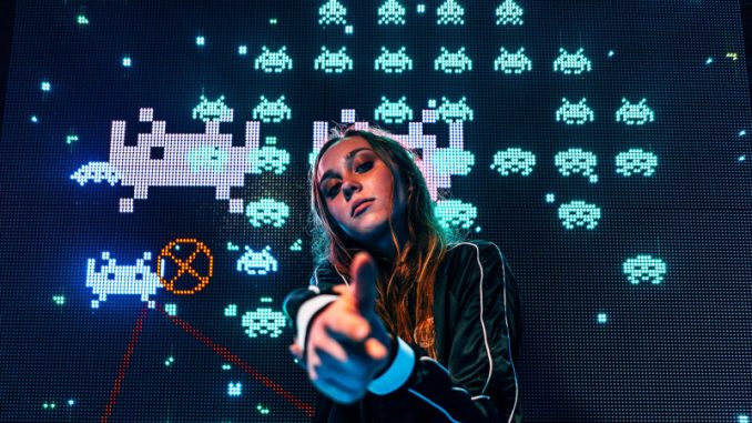 label-beat-drop-gaming-musique-pubg-mobile La DJ Mariana BO ayant travaillé avec le label Beat Drop postée devant l’écran d’une version du jeu Space invaders