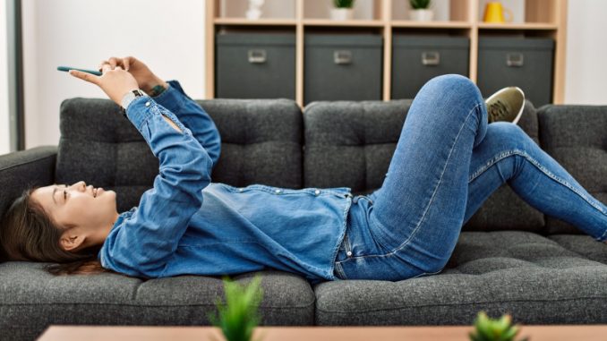 femmes-jeux-video-smartphone Une femme allongée sur un divan et en train de jouer à des jeux vidéo sur son smartphone