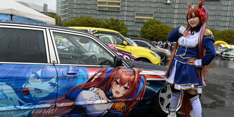 Une Japonaise en cosplay devant une voiture véhiculant la culture Itasha, ornée du personnage d’animé Daiwa Scarlet qu’elle incarne.