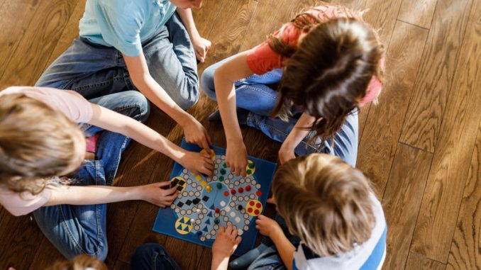 jeux-de-societe-bienfaits-apprentissage-mathematiques De jeunes enfants en train de jouer à des jeux de société, à même le sol.