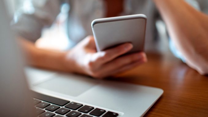 onlyfans-profit-createurs-contenus-gaming Une femme, devant son bureau, en train de suivre un créateur de contenus d’OnlyFans sur son smartphone.