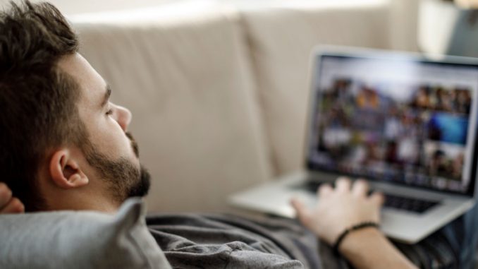 baisser-la-qualite-des-videos-sauver-la-planete Un homme sur son canapé en train de visionner des contenus gaming et qui a pris la peine de baisser la qualité des vidéos pour préserver la planète.