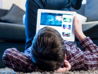 Un jeune garçon en train de regarder sa tablette dans son salon, expérimentant les effets des jeux vidéo sur le cerveau ainsi que des écrans.