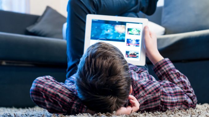 effets-des-jeux-video-sur-le-cerveau-des-enfants Un jeune garçon en train de regarder sa tablette dans son salon, expérimentant les effets des jeux vidéo sur le cerveau ainsi que des écrans.