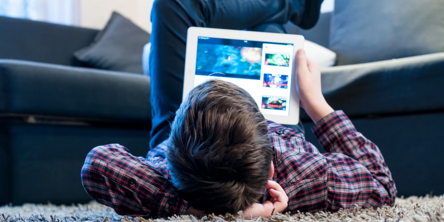 Un jeune garçon en train de regarder sa tablette dans son salon, expérimentant les effets des jeux vidéo sur le cerveau ainsi que des écrans.