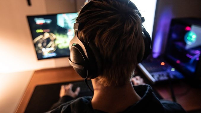 Rear View of Gamer with Headset on Playing Online Video Games in Dark Room - stock photo Vue de dos d’un gamer jouant a un jeu video portant un casque audio