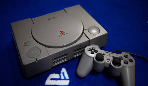 anniversaire Playstation Une console PlayStation grise avec sa manette classique sur une table.